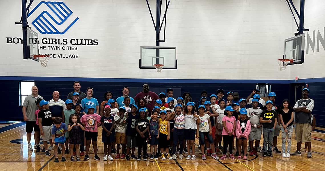 A large group of children and adults sanding in a backetball court within a Boy and Girls Club location.